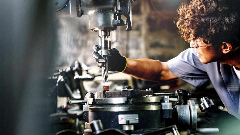 Mitarbeiter bedient eine Metallbearbeitungsmaschine in einer industriellen Produktionsumgebung.