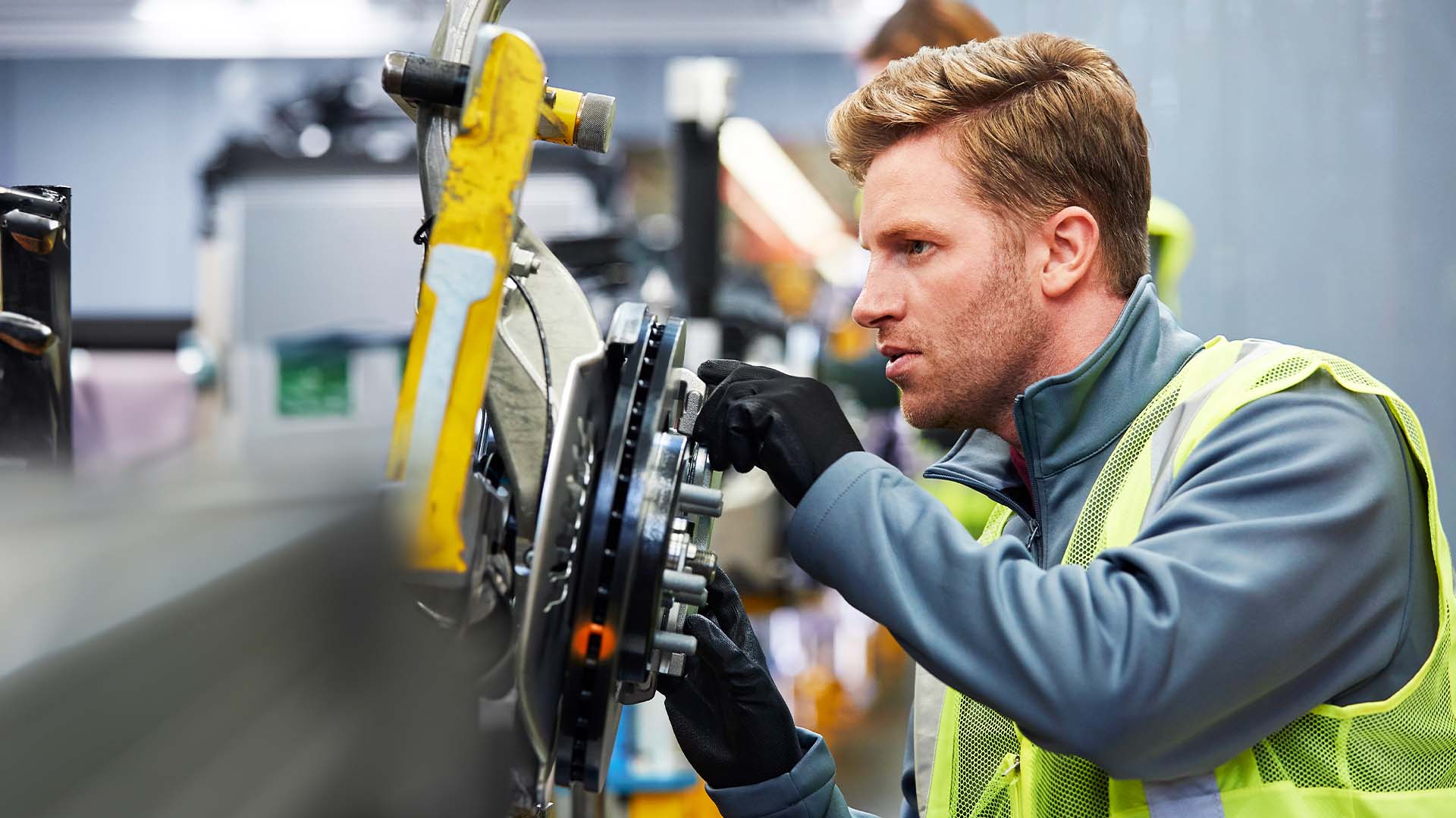 Mitarbeiter mit Warnweste prüft eine Maschine in der industriellen Fertigung.